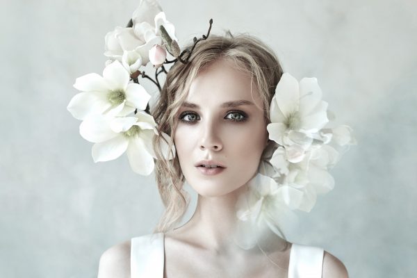 Perfect bride with jewels, a portrait of a girl in a long white dress. Beautiful hair and clean delicate skin. Wedding hairstyle blonde woman. Girl with a white flower in her hands